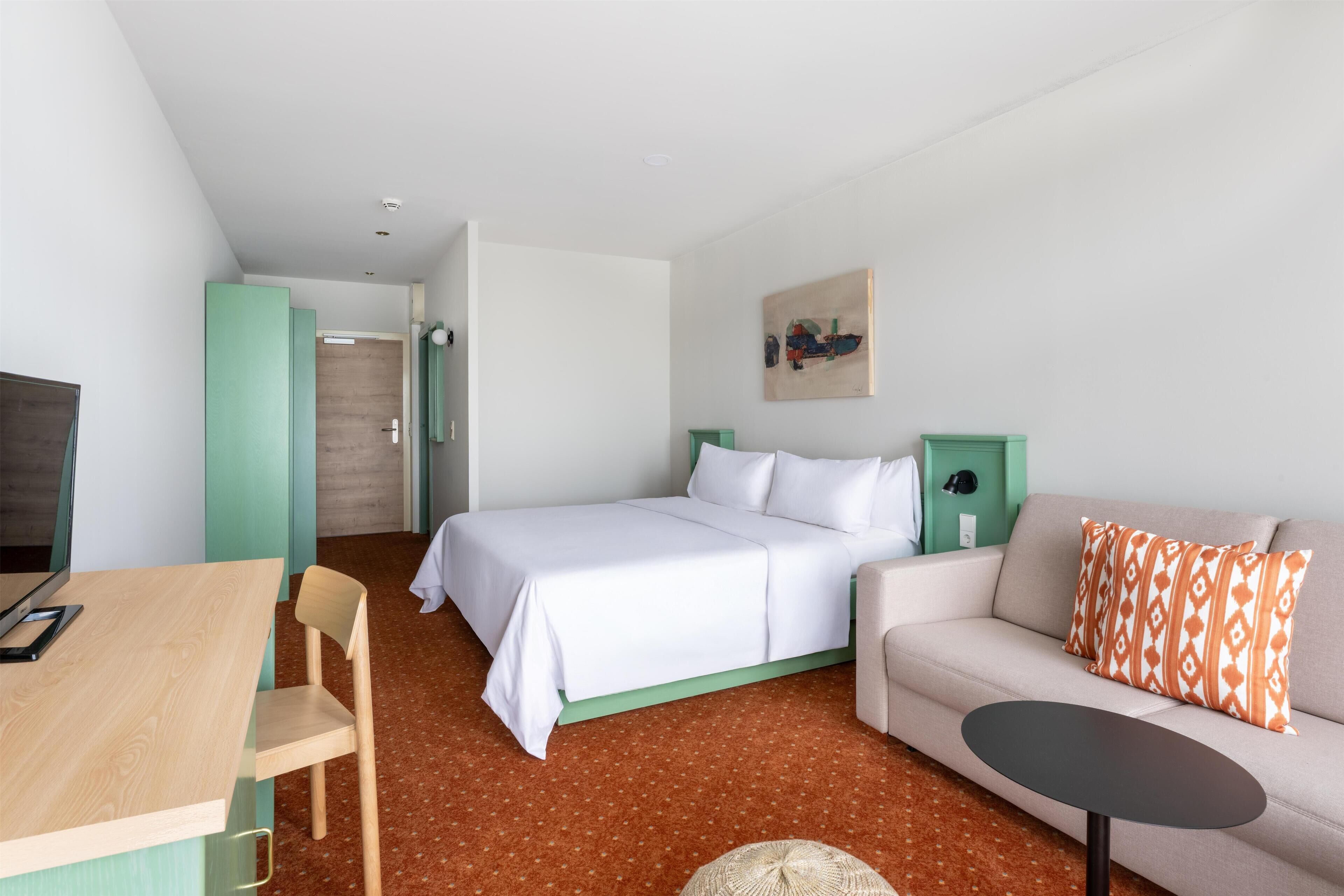 Ein modernes Hotelzimmer mit einem Bett, einer Couch, einem kleinen Tisch und einem Schreibtisch.