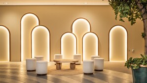A lobby with a round wooden table surrounded by white cushioned stools, a potted plant, and illuminated wall panels. - IFA Schöneck, Hotel & Ferienpark (Schoeneck)