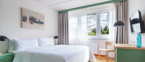 A hotel room with a bed, a desk, a chair, a TV, and a window with curtains.