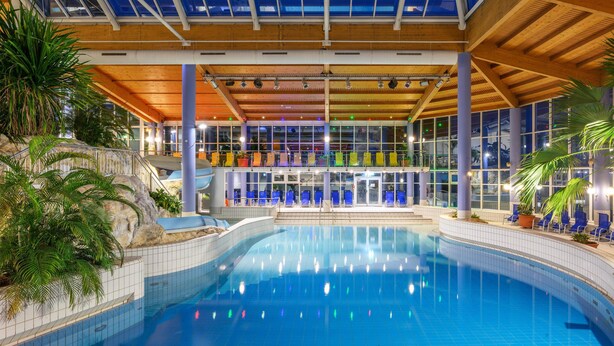 An indoor swimming pool with a glass ceiling, blue chairs, and potted plants. - IFA Schöneck, Hotel & Ferienpark (Schoeneck)