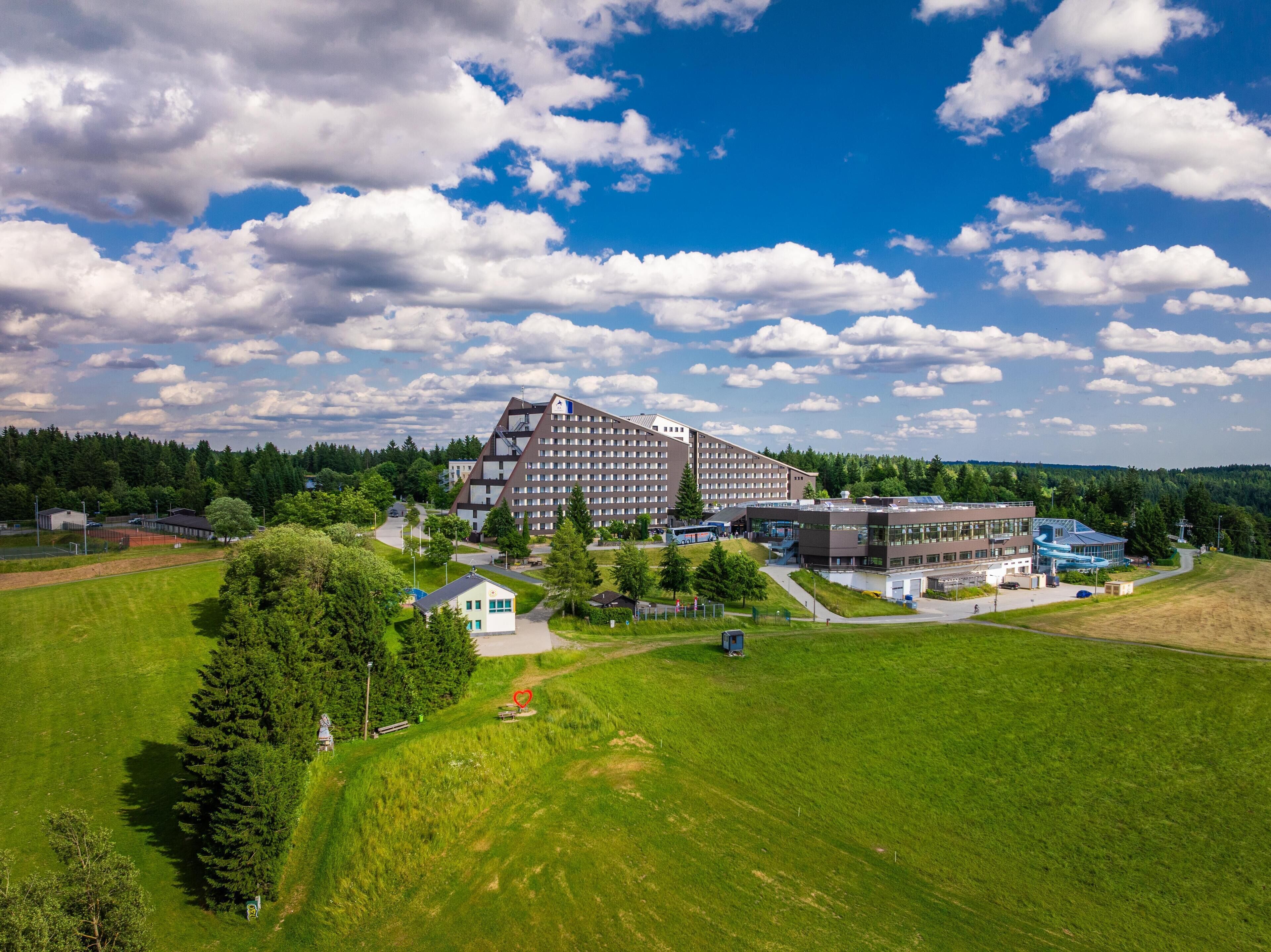 A large hotel with multiple buildings, surrounded by green fields and trees.