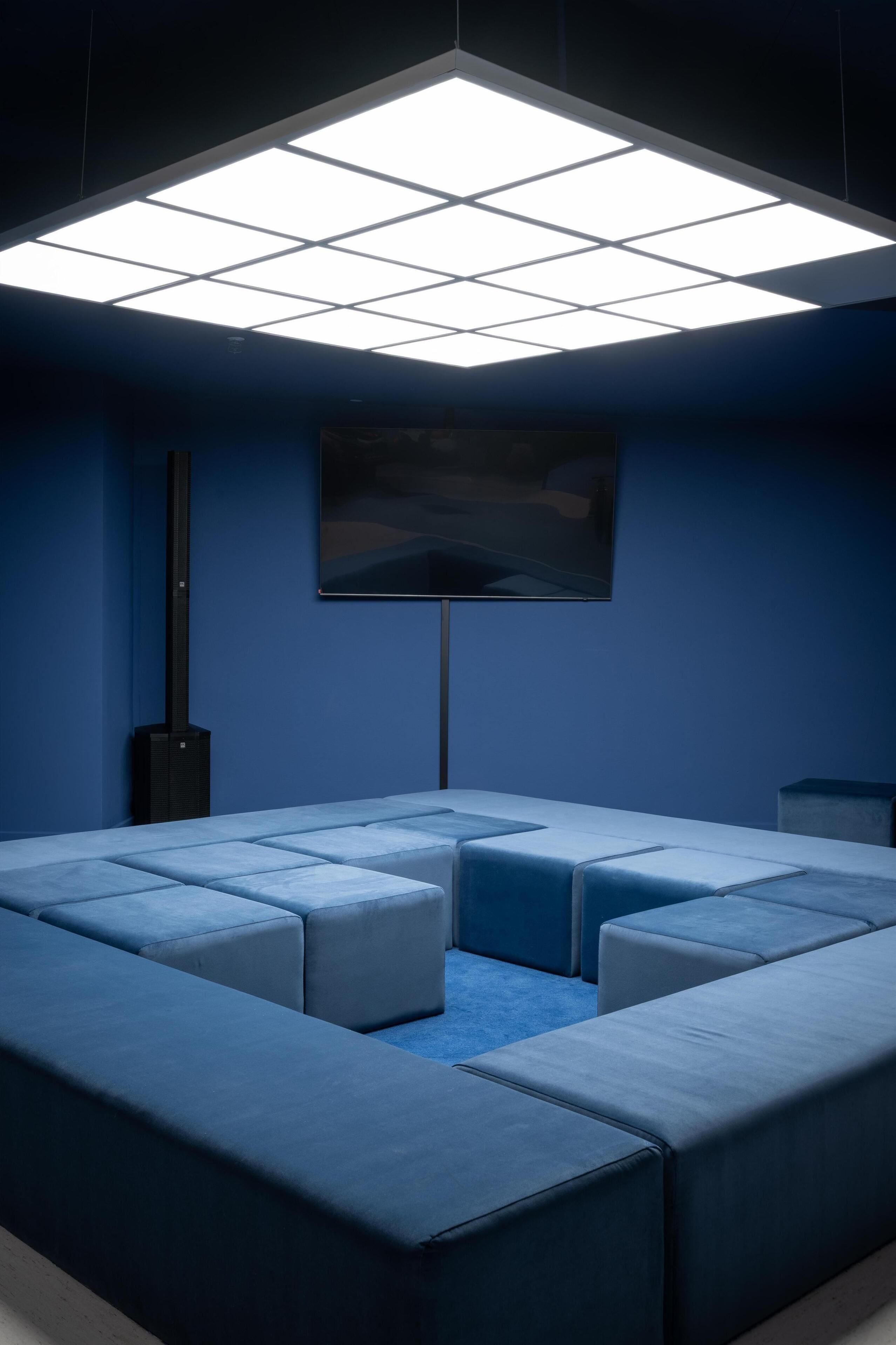 Una habitación moderna con un sofá modular, un televisor de pantalla plana montado en la pared y una lámpara de techo.