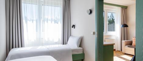 Habitación de hotel con dos camas, un escritorio, una silla y vistas al exterior.
