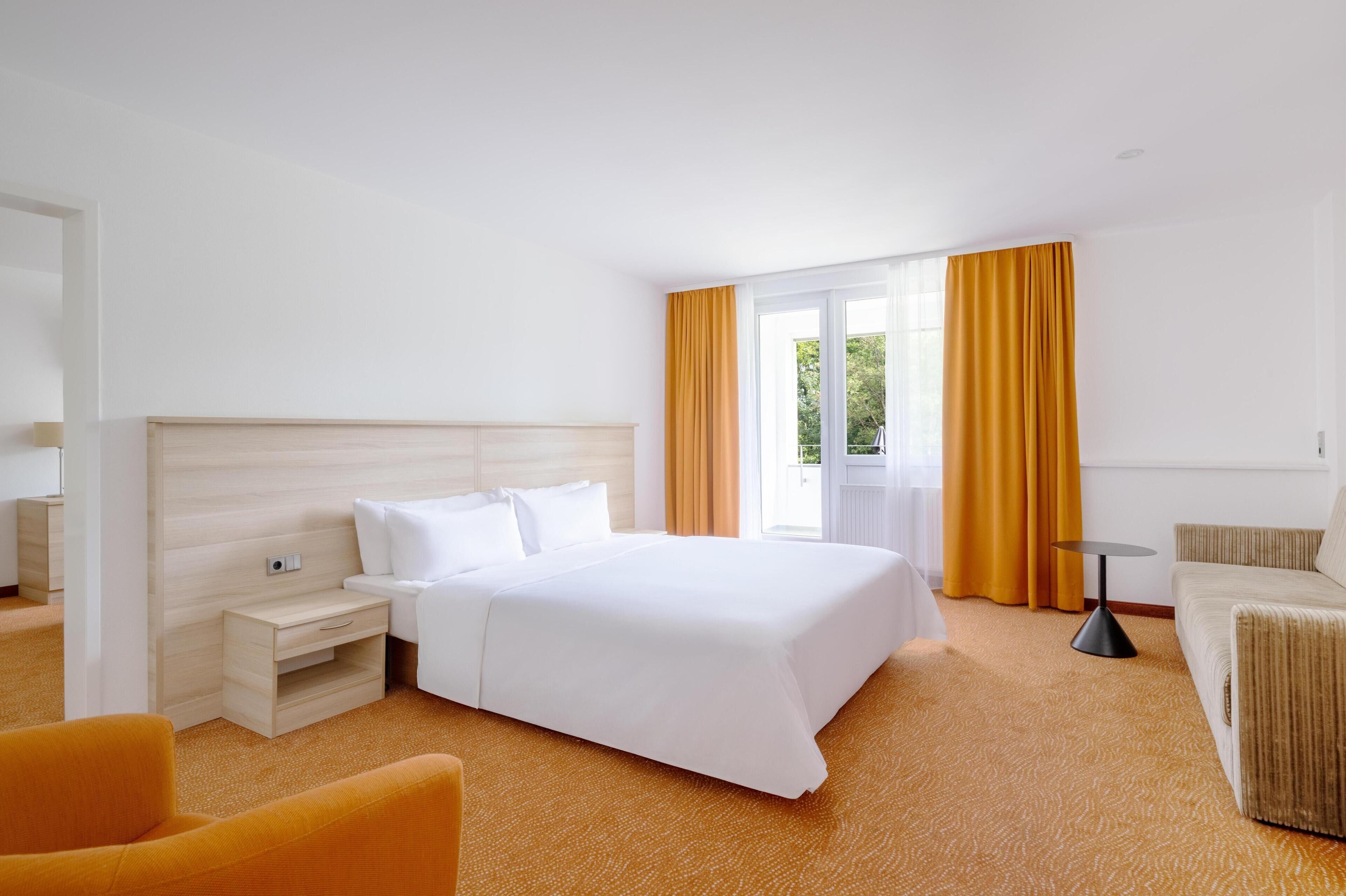 A hotel room with a large bed, a wooden nightstand, a small table, and a sofa.
