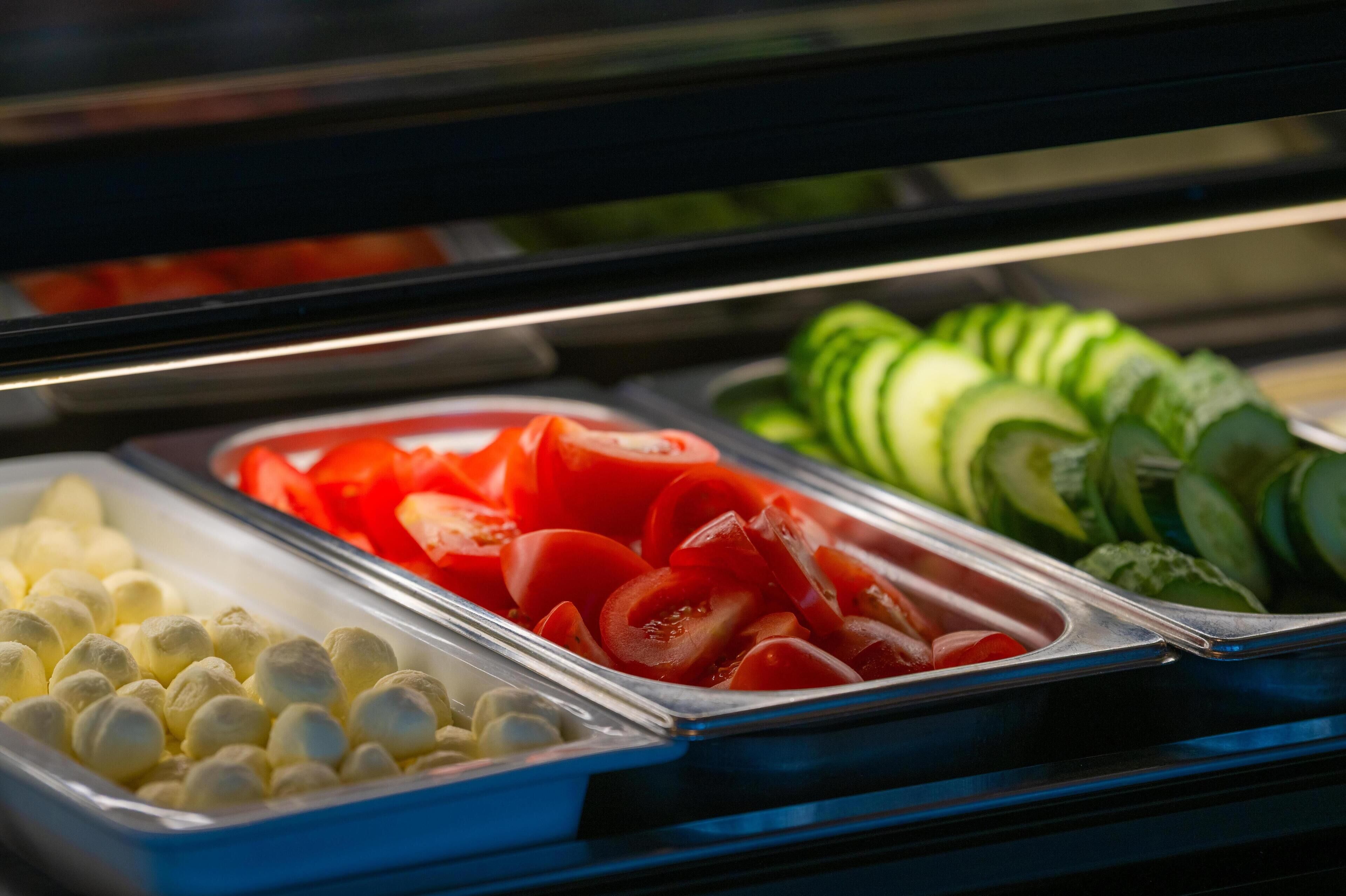 A buffet with various food items including sliced tomatoes, cucumbers, and other vegetables.