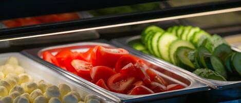 A buffet with various food items including sliced tomatoes, cucumbers, and other vegetables.