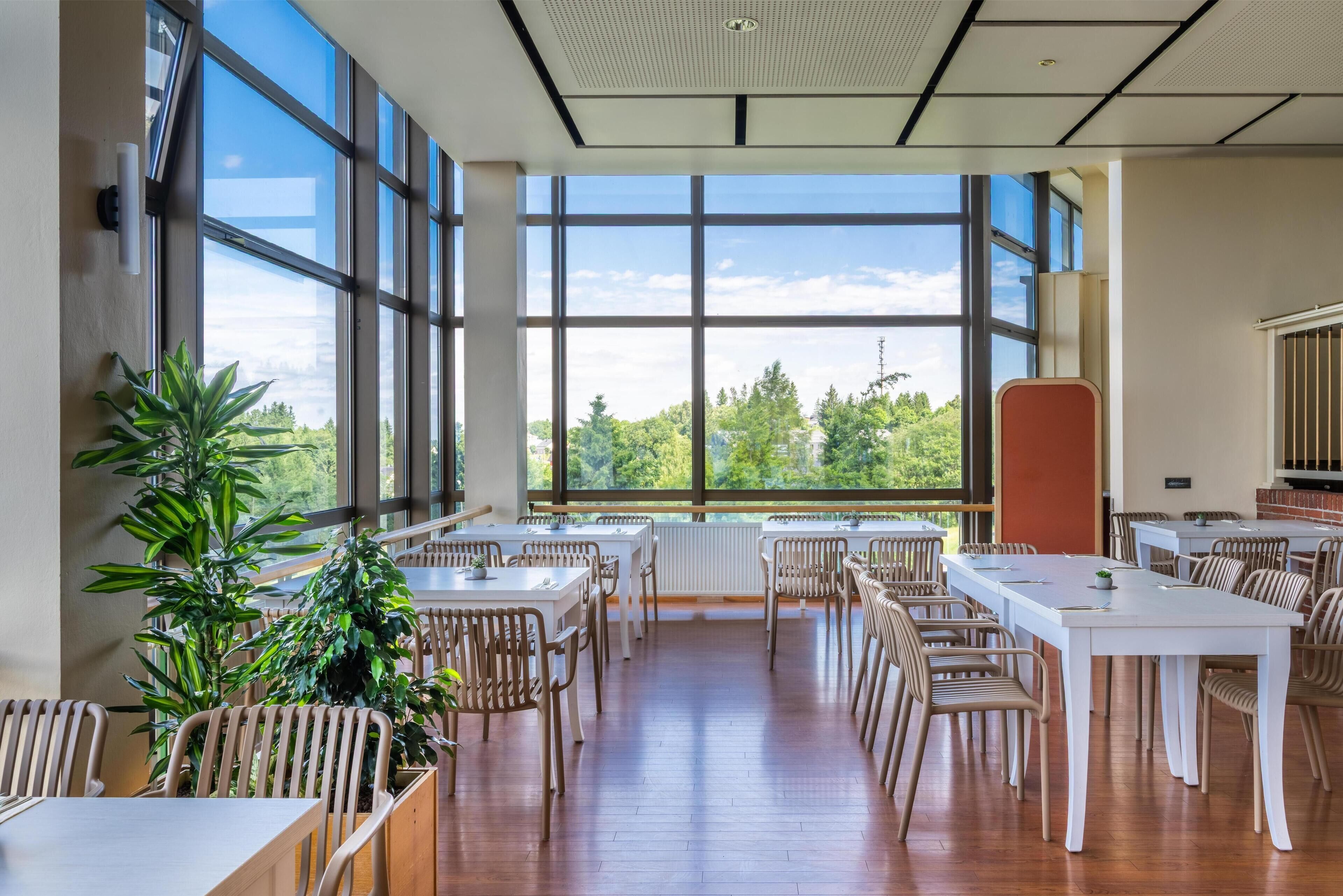 Un comedor espacioso con ventanas amplias, suelo de madera y varias mesas y sillas.