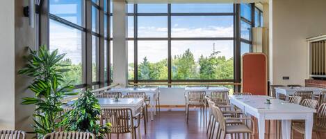 A spacious dining area with large windows, wooden flooring, and multiple tables and chairs.