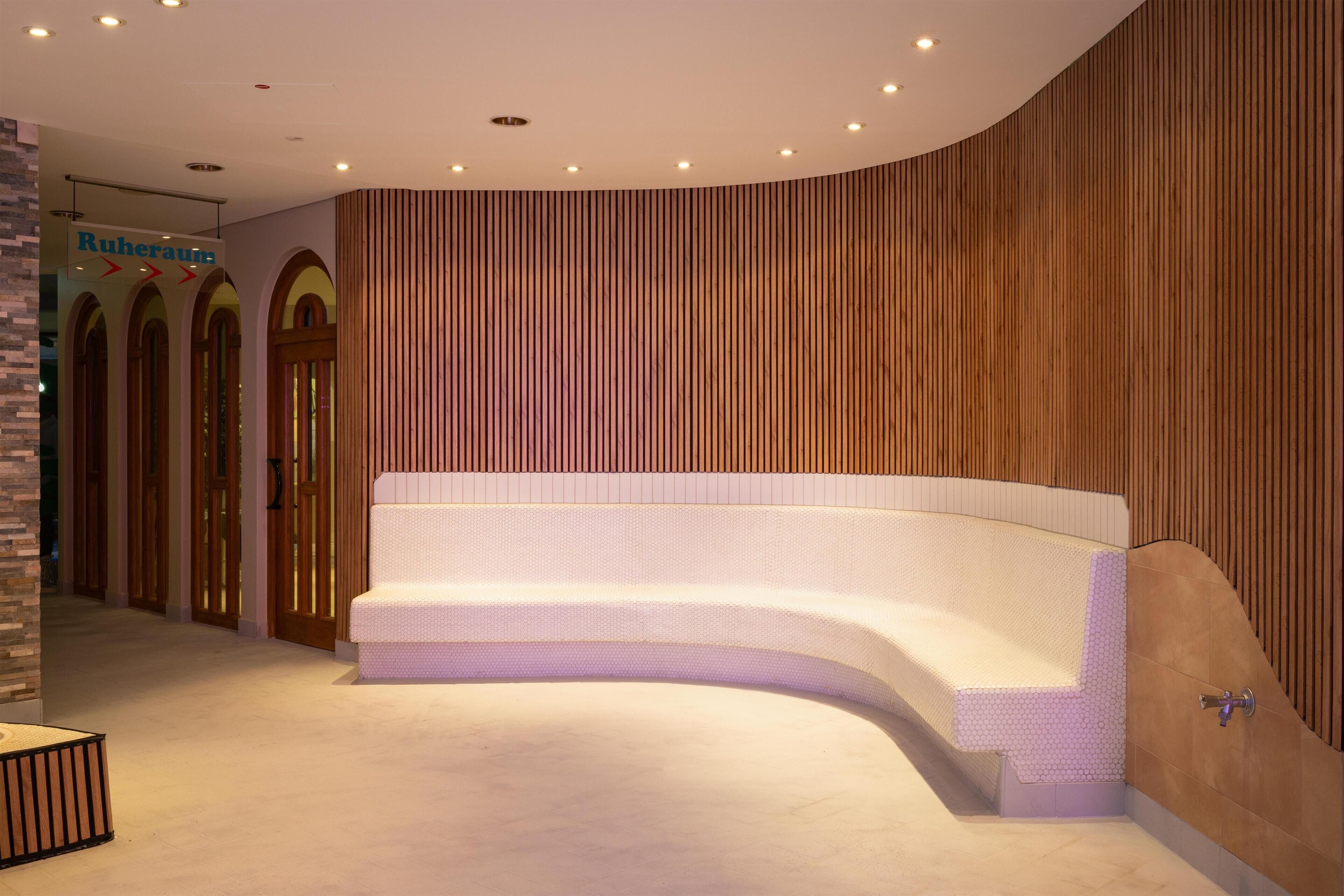 A modern hotel lobby with a curved white bench, wooden panel walls, and a sign reading "Ruheraum".