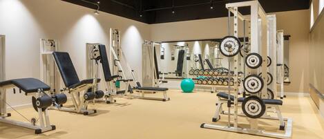 Ein Fitnessstudio mit verschiedenen Trainingsgeräten, darunter Kraftgeräte, Kurzhanteln und einer Spiegelwand.