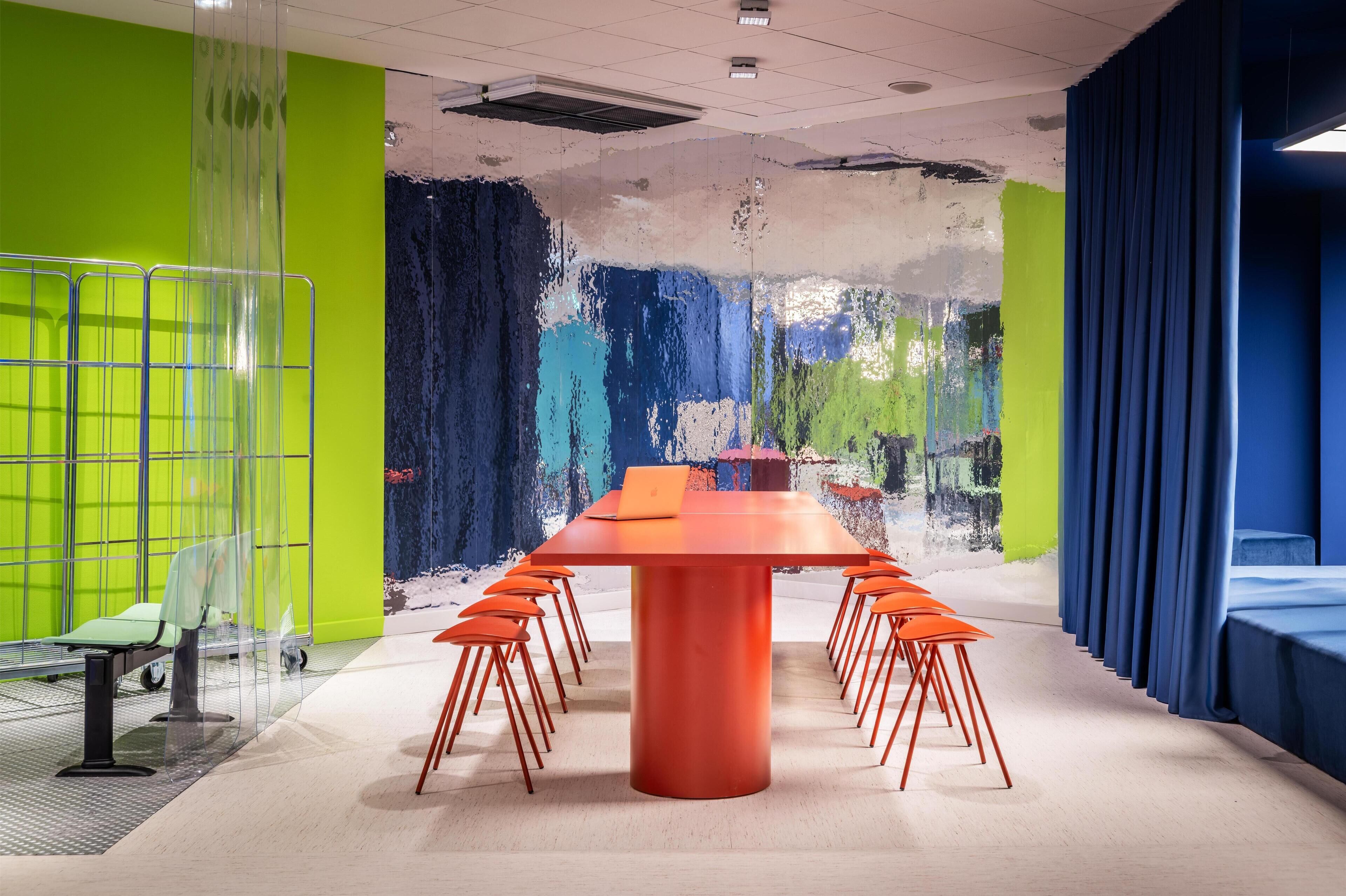 A conference room with a long table, orange chairs, and a laptop on the table.