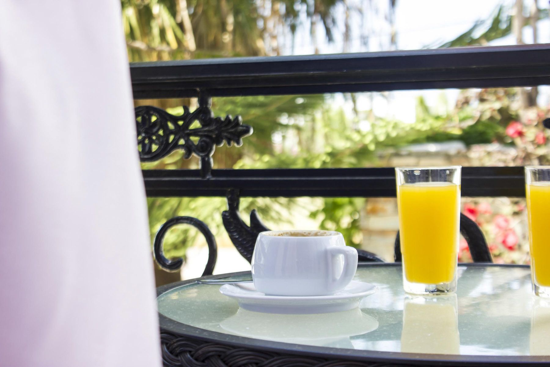 A table with a white cup and saucer, and two glasses of orange juice.