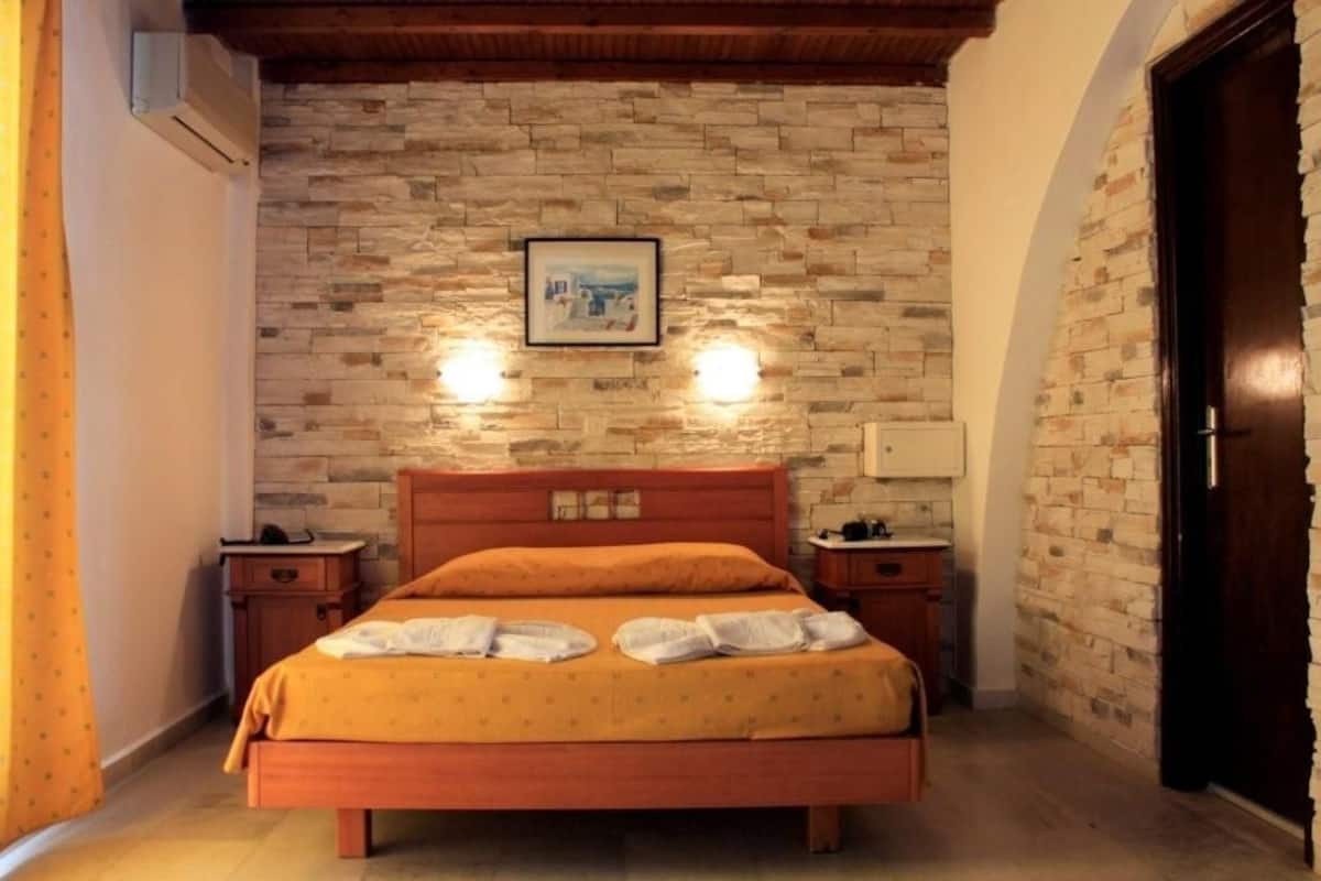 A bedroom with a stone wall, a wooden bed, two bedside tables, and a framed picture on the wall.