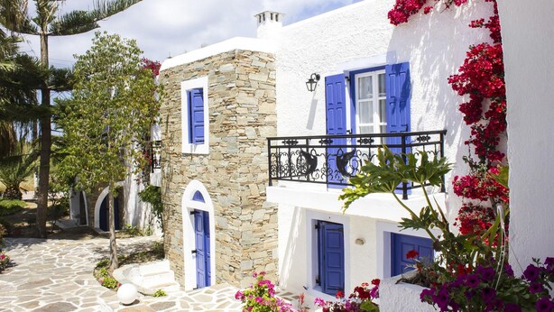 A traditional white building with blue shutters and stone walls, featuring a stone-paved courtyard and lush greenery. - Naxos Holidays (Naxos)