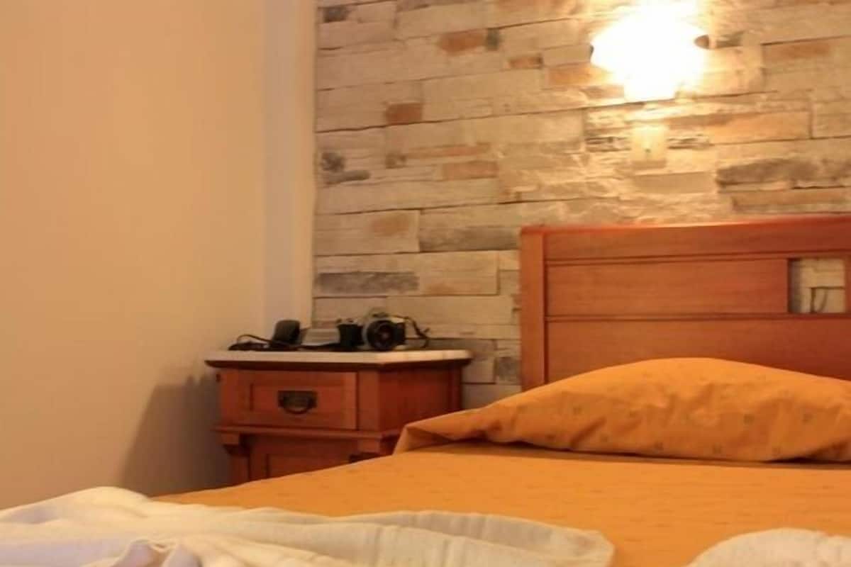 A bedroom with a stone wall, a wooden headboard, and a bedside table with a lamp.