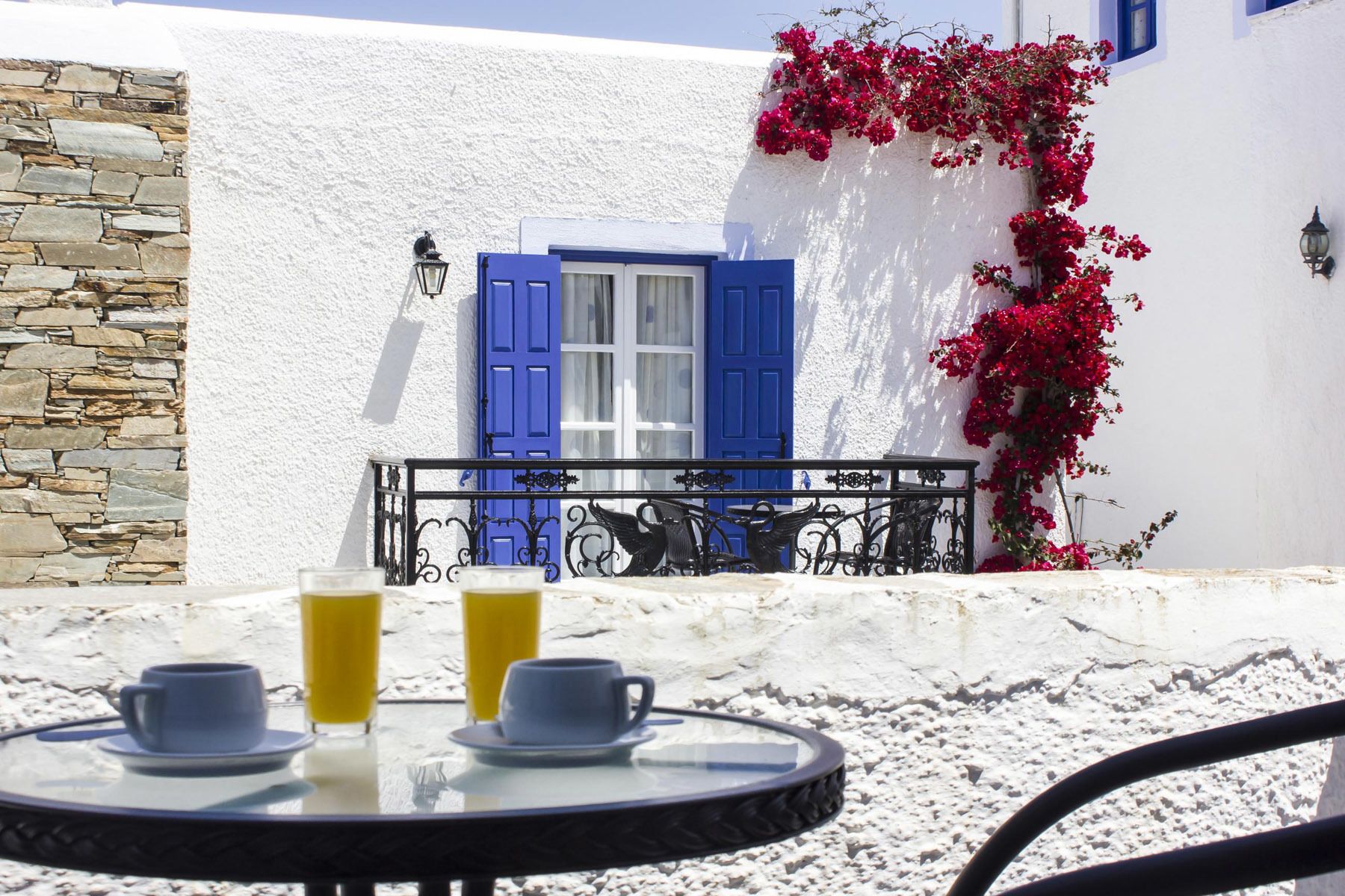 A round table with two cups and two glasses of orange juice, set against a white wall with a stone facade and a blue door.