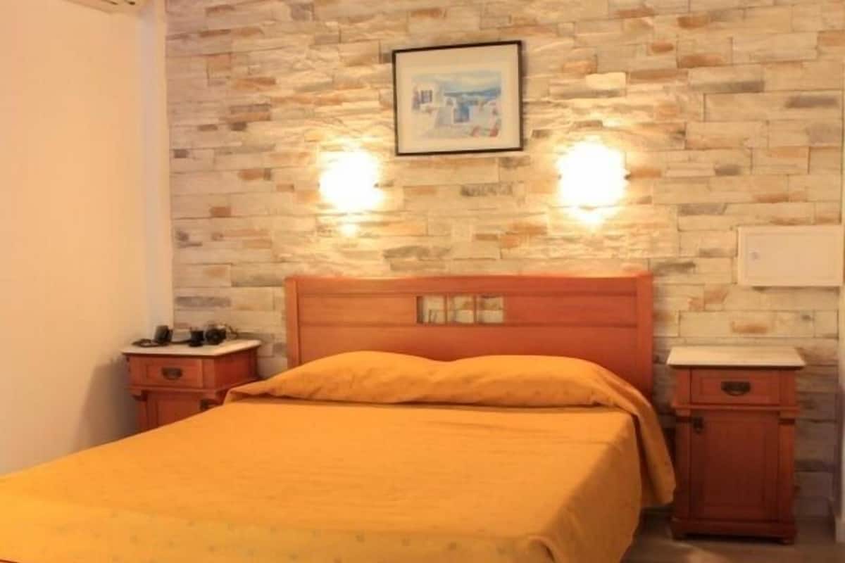 A bedroom with a wooden bed, two bedside tables, a stone wall, and a framed picture.