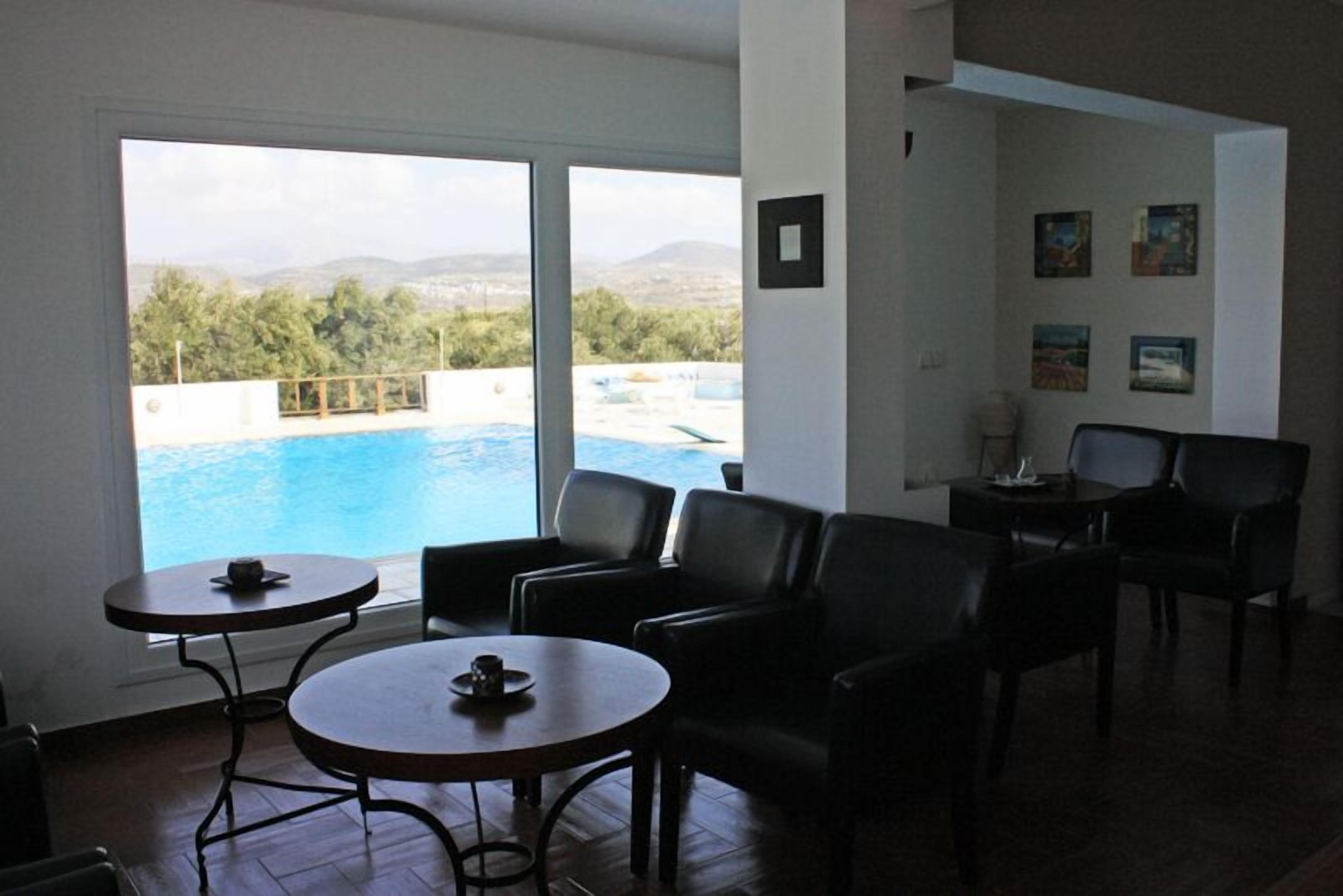 Una sala con vistas a una piscina y montañas. Hay dos mesas redondas y cuatro sillas.