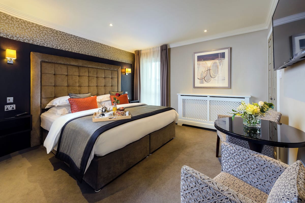 A hotel room with a large bed, a bedside table, a small table with a vase of flowers, and a chair.