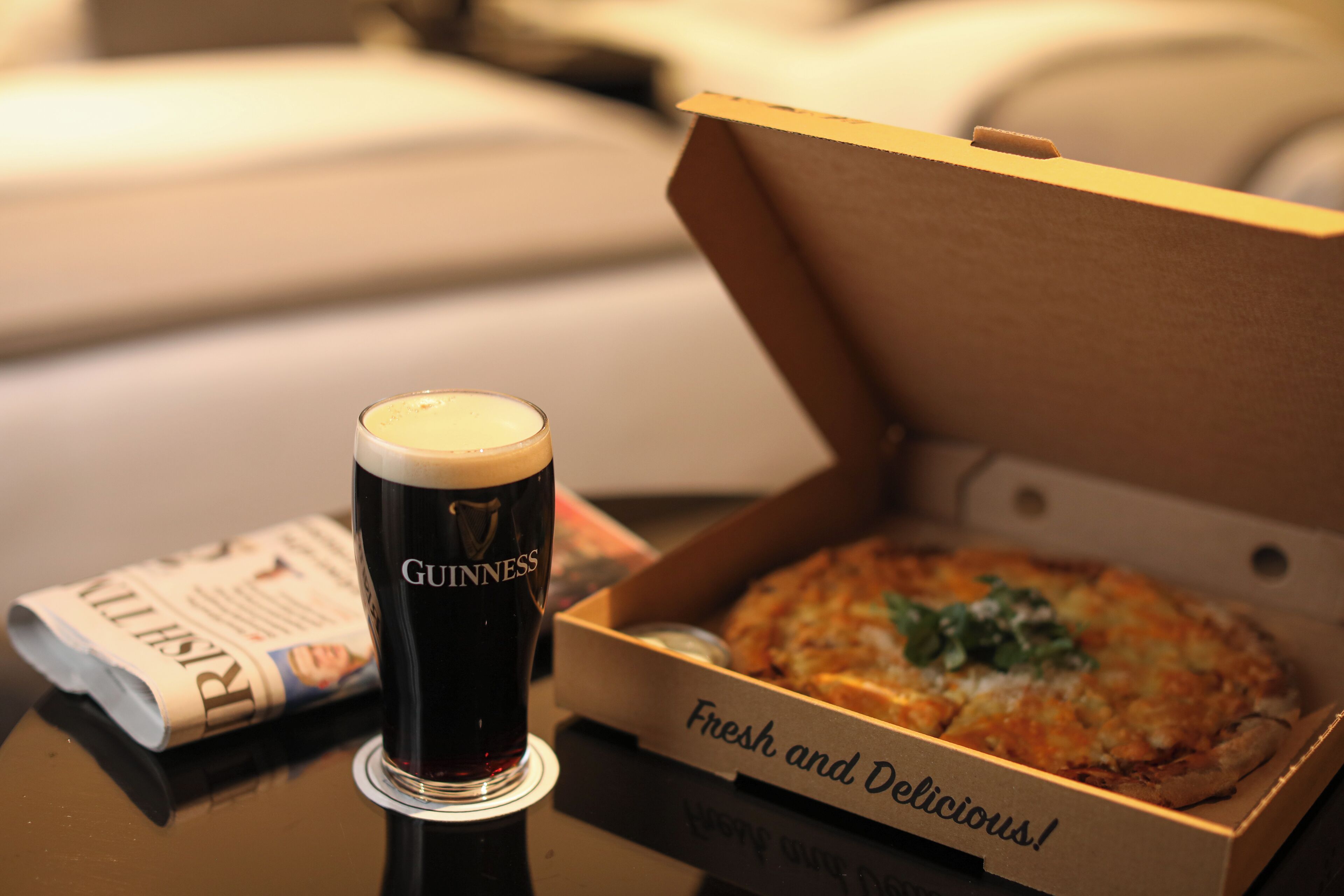 A glass of Guinness beer and a pizza box labeled "Fresh and Delicious!" on a table.