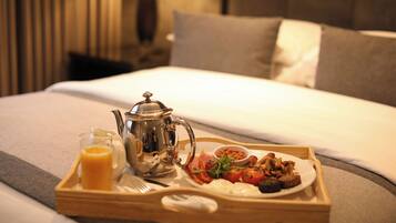 A breakfast tray with a teapot, a glass of orange juice, and a plate of food on a bed.