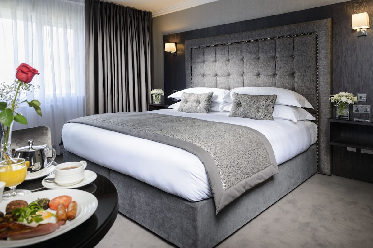 A modern hotel room with a large bed, a bedside table with a lamp, and a breakfast tray.
