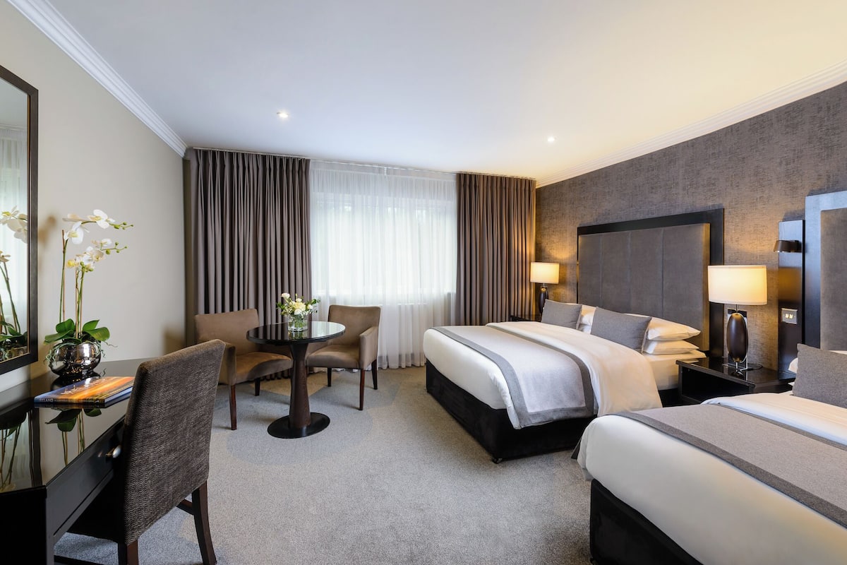 A hotel room with a large bed, a desk with a chair, a small table with a chair, and a large mirror.