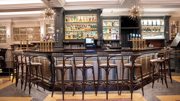A bar area with a curved counter, multiple stools, and a variety of bottles on shelves. - Killarney Oaks Hotel (Killarney)