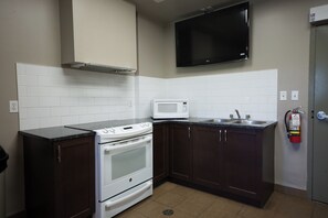 A compact kitchen with white appliances, a microwave, a stove, dark cabinets, a sink, and a fire extinguisher. - Residence & Conference Centre - Windsor (Windsor)