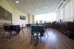 Un salón de conferencias con una gran mesa, sillas, una televisión y una zona de cocina con armarios y electrodomésticos.