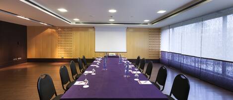 A conference room with a long table, chairs, a projector screen, and a large window.