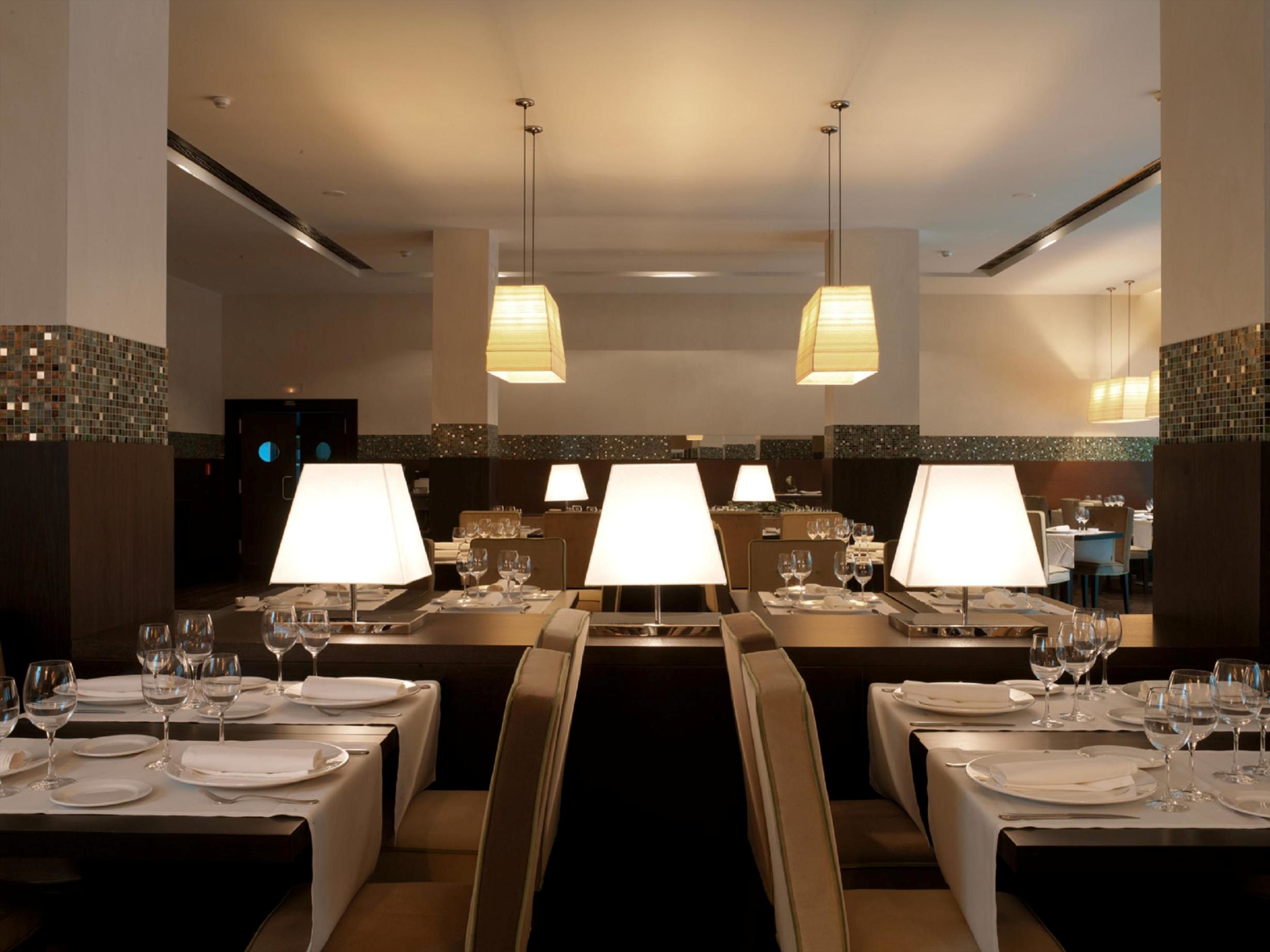 Un restaurante con varias mesas, cada una dispuesta con manteles blancos, platos y copas de vino.