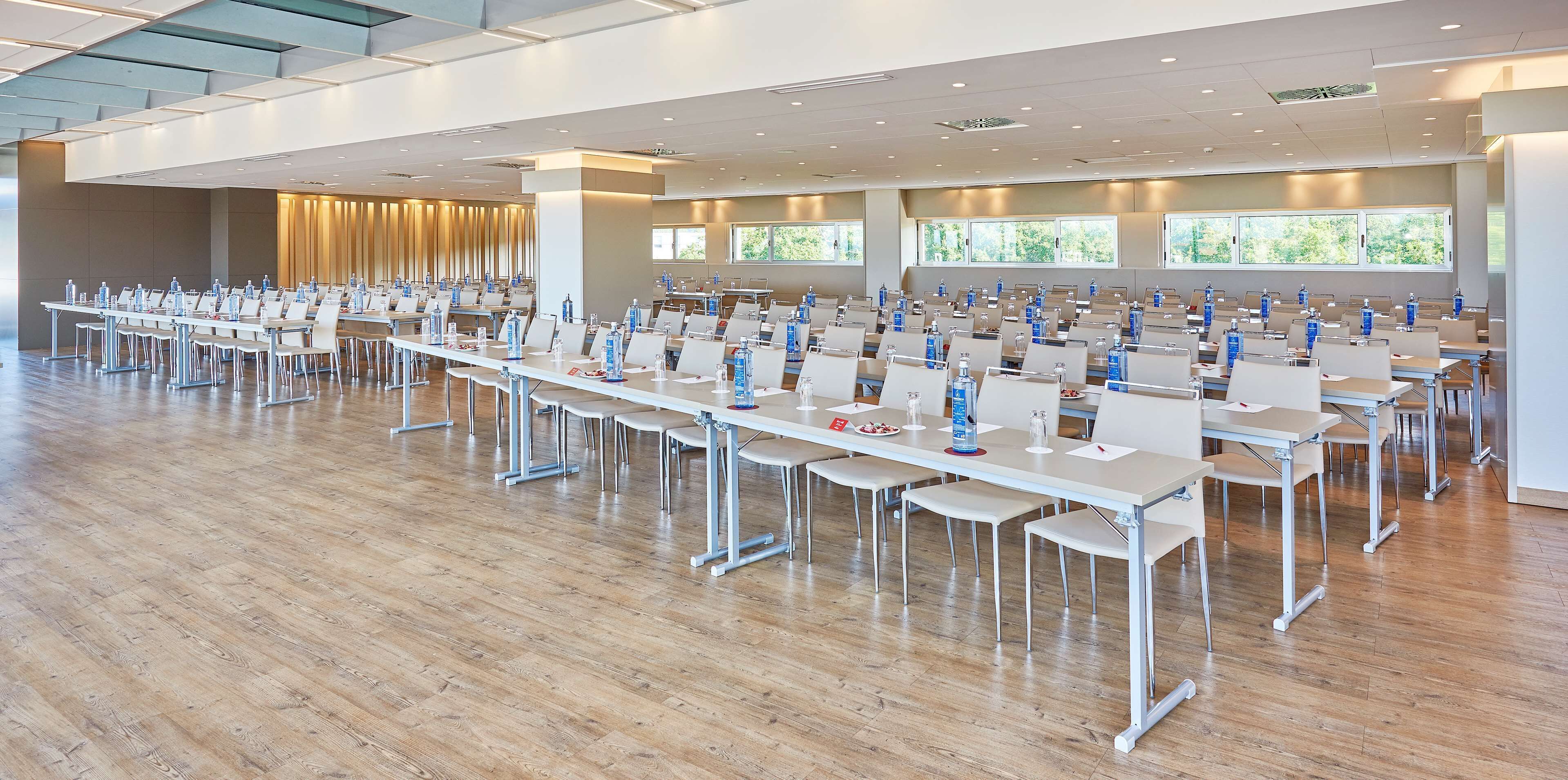 Un salón de conferencias amplio con filas de mesas y sillas, equipado con botellas de agua y placas de identificación.