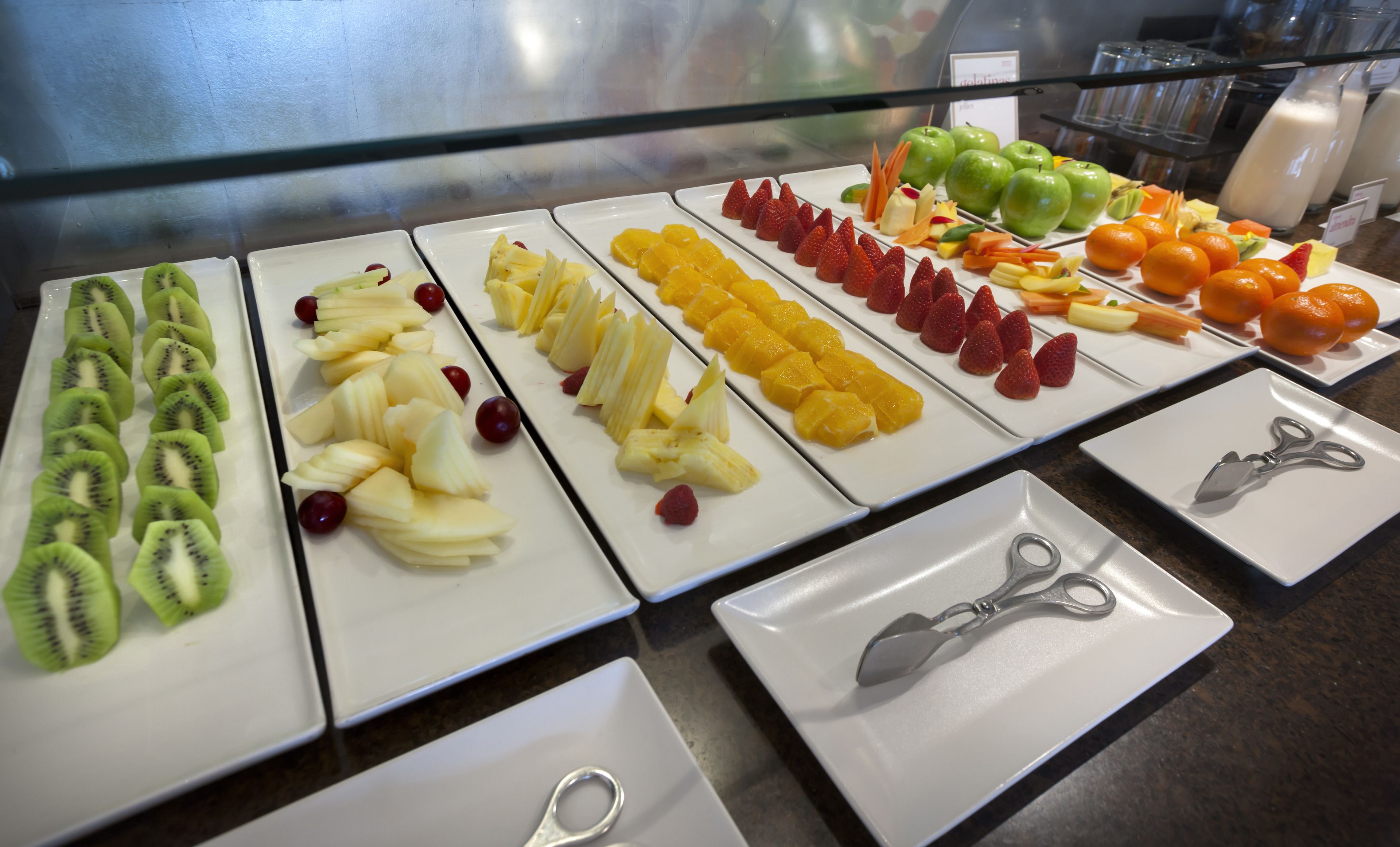 A fruit display with various sliced fruits and a pair of scissors on a counter.