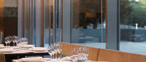 A restaurant with tables set for dining, large windows, and hanging lamps.