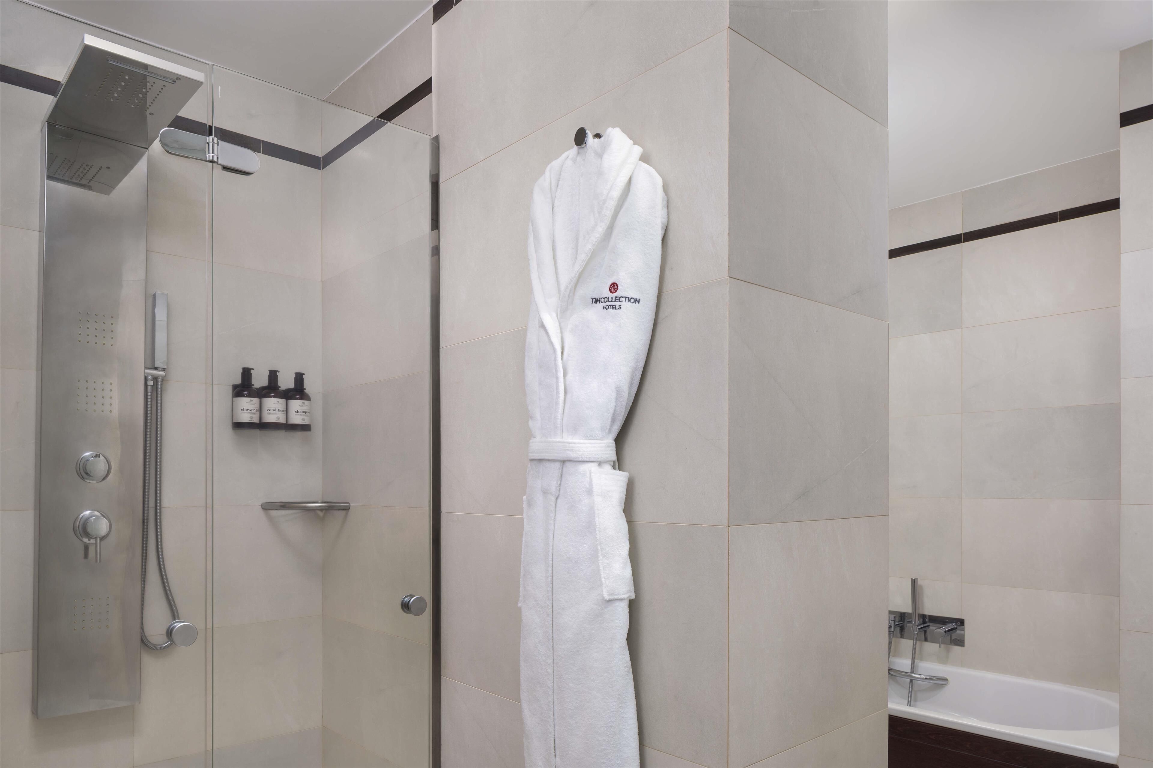 Un bagno moderno con doccia a vetro, un accappatoio bianco appeso al muro e una vasca da bagno.