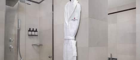 Un baño moderno con cabina de ducha de vidrio, una bata blanca colgada en la pared y una bañera.