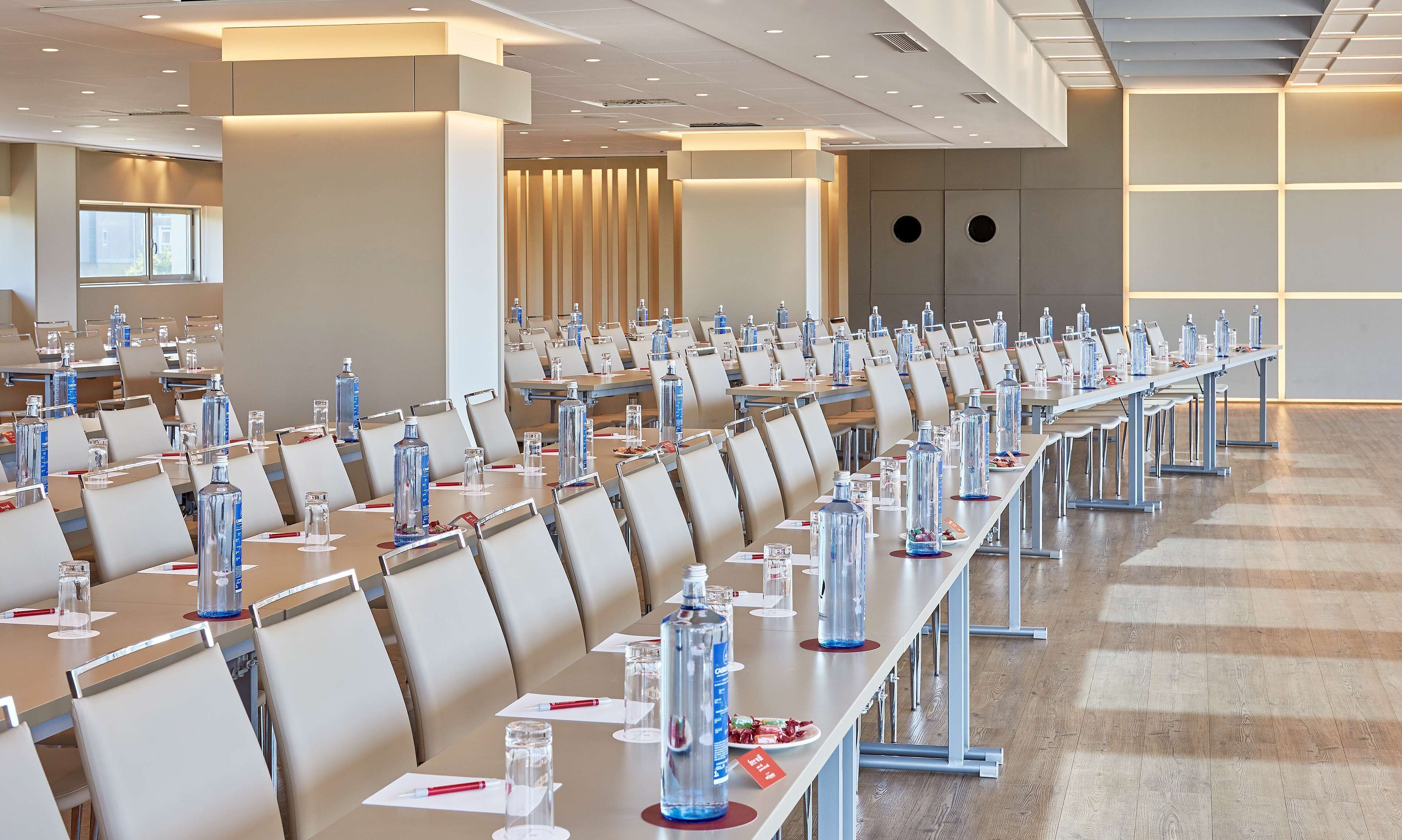 A conference room with rows of tables, chairs, and water bottles.