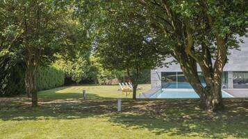 A well-maintained lawn with a swimming pool, surrounded by mature trees and a modern building.