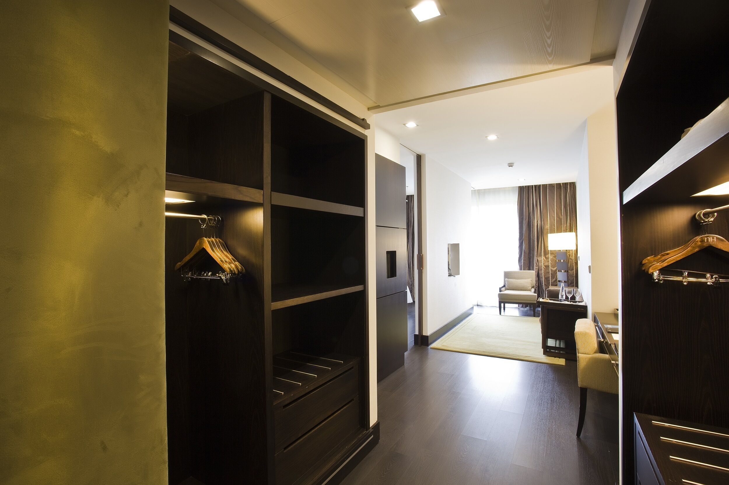 Hotelkamer met inloopkast, zithoek met een bank en fauteuils, en uitzicht op de gang.