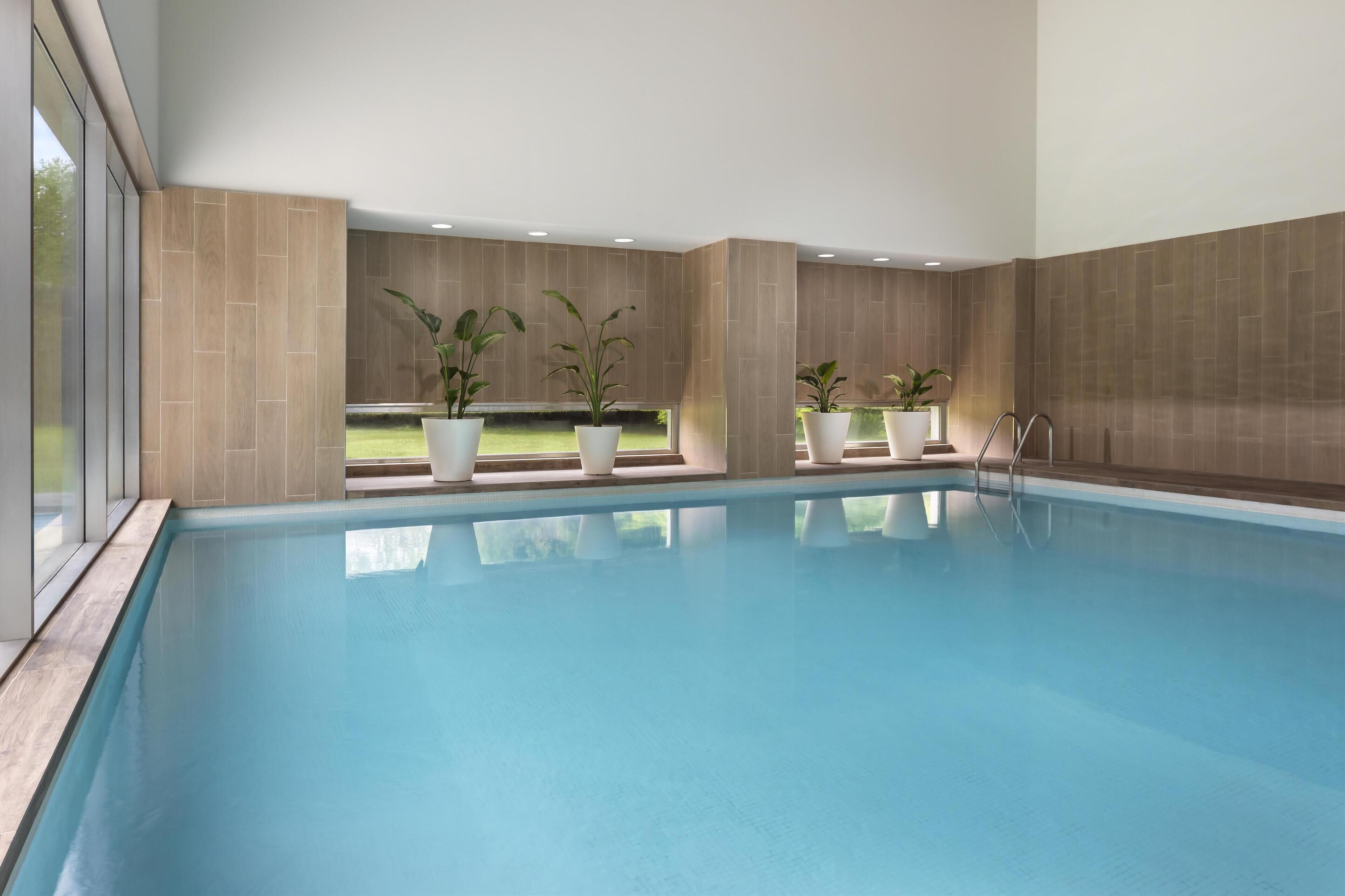 A swimming pool with clear blue water, surrounded by beige tiled walls and large windows.