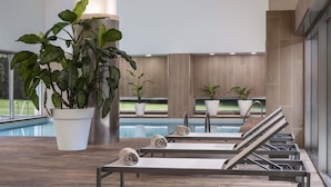 A modern indoor pool area with lounge chairs, potted plants, and a view of the outdoor pool.