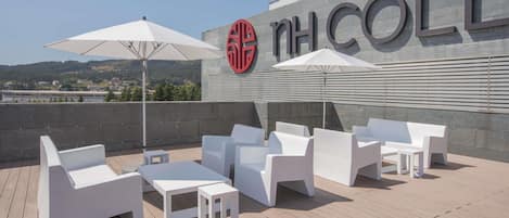 Una terraza en la azotea con muebles blancos y sombrillas, un cartel con