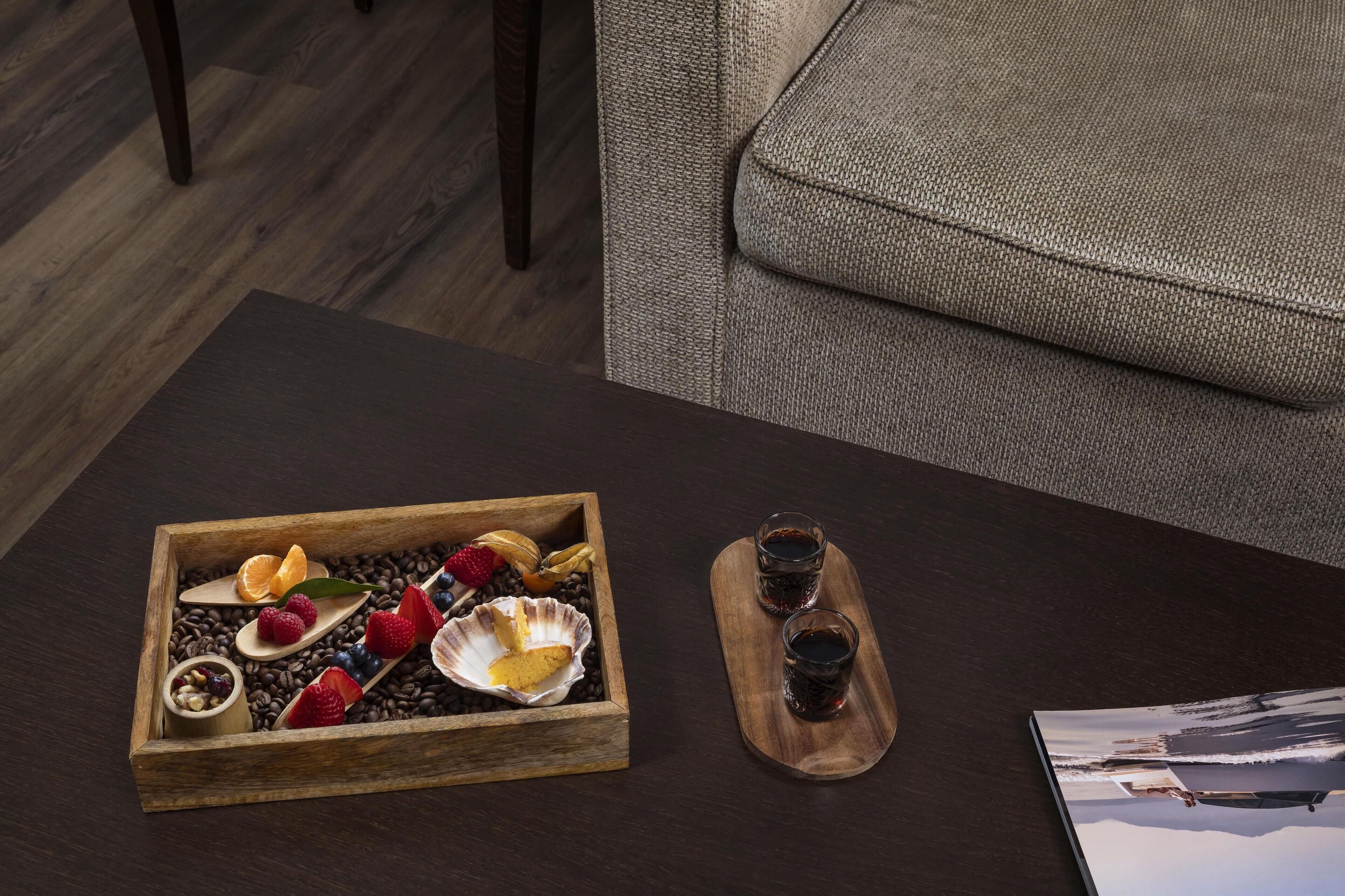 A wooden tray with fruits and coffee beans on a table, next to a couch and a picture frame.