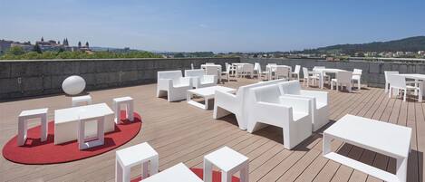 A rooftop terrace with white furniture, a red carpet, and a view of a cityscape.