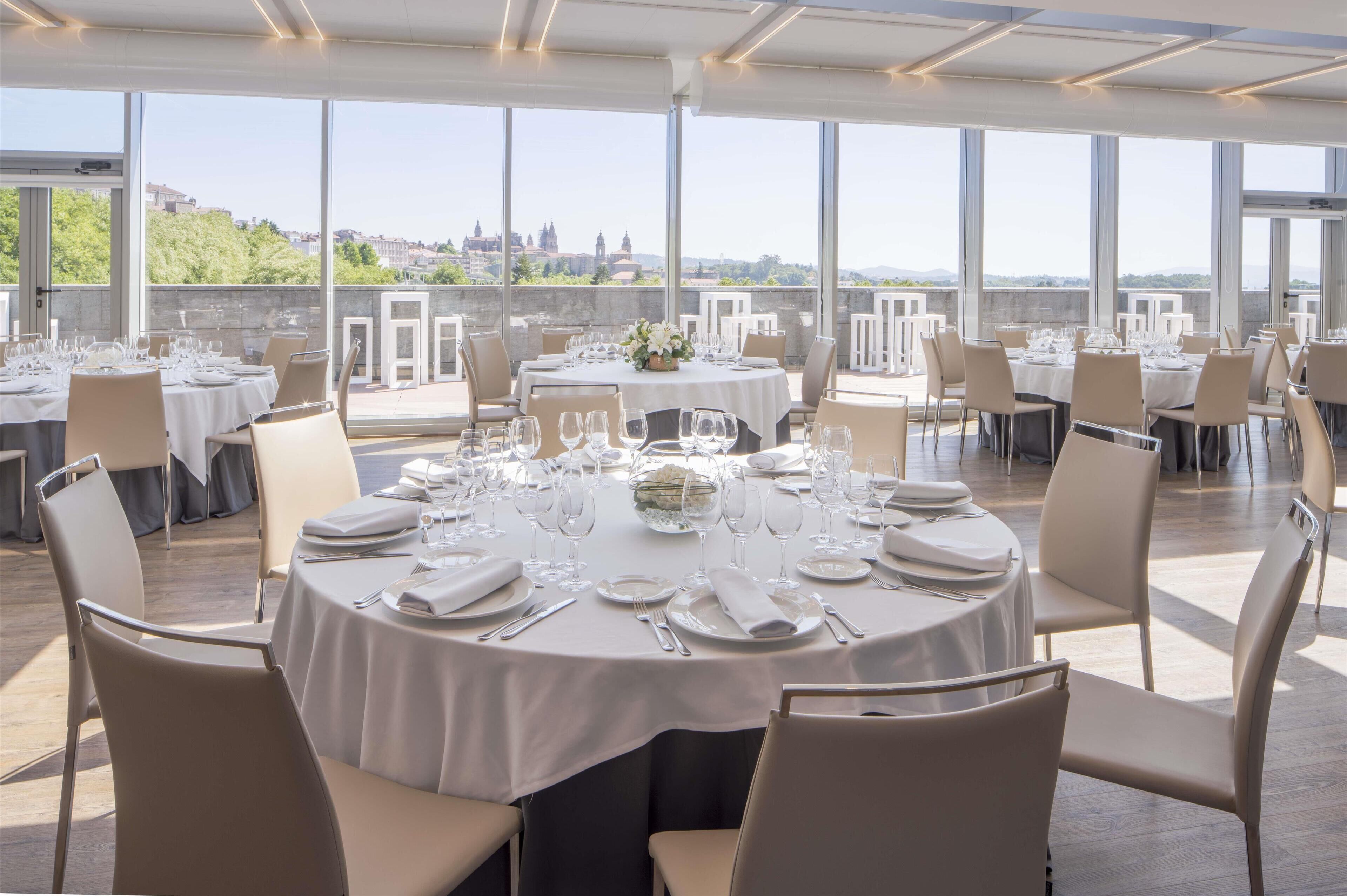A restaurant with round tables set for dining, large windows offering a view of a cityscape.