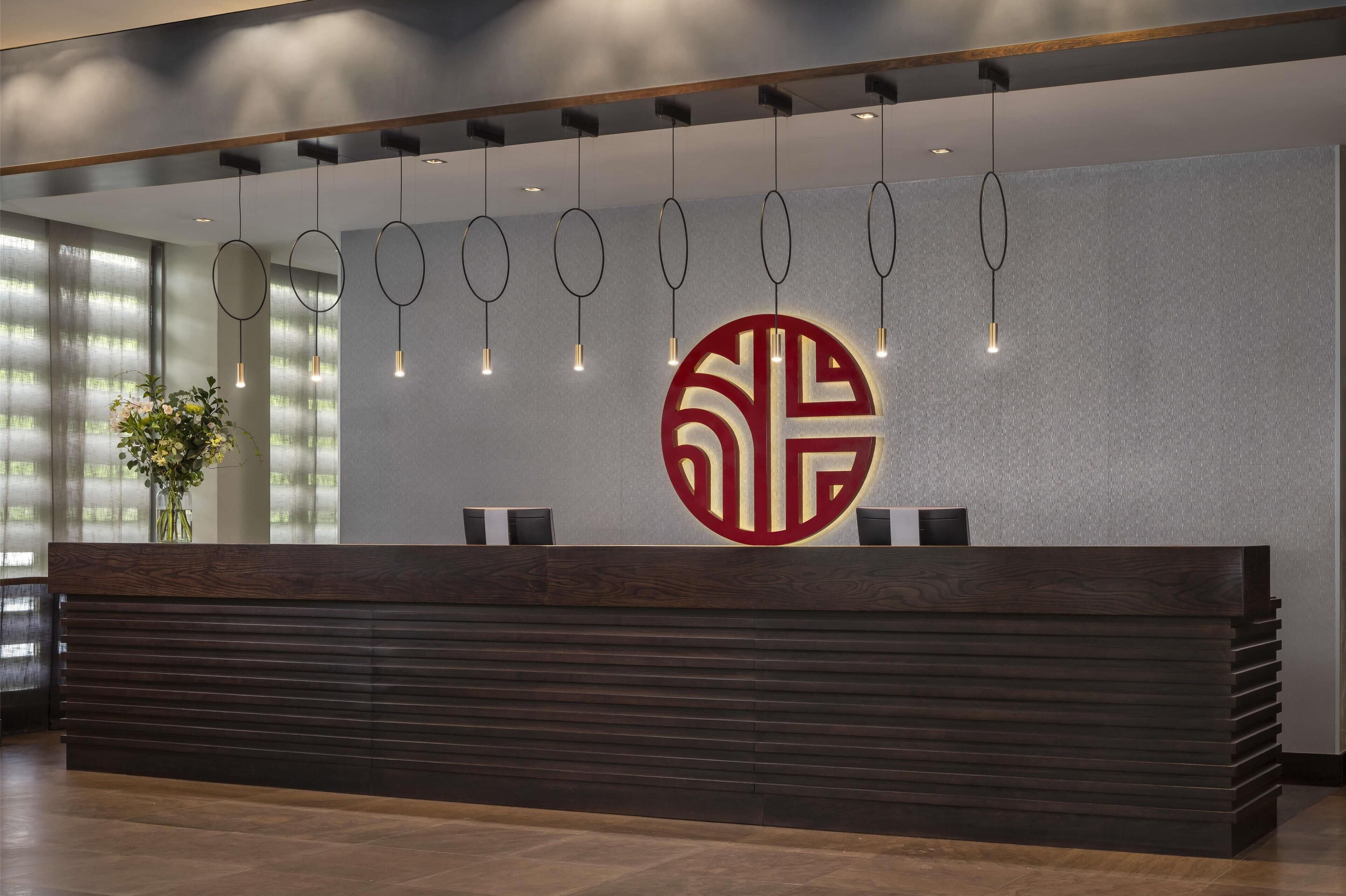 Un mostrador de recepción de diseño moderno, con un amplio logotipo en la pared e iluminación colgante en el techo.
