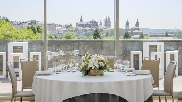 A dining area with a table set for six, overlooking a cityscape with historic buildings.