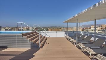 Un área de piscina en la azotea con vistas a la ciudad, incluyendo edificios y montañas a lo lejos.