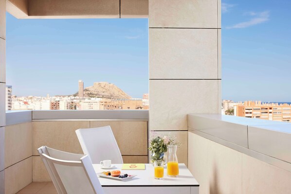 Un balcón con una mesa dispuesta para el desayuno, una silla, un jarrón con flores y vistas a la ciudad y a las montañas.